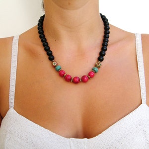 Puede incluir: Un collar de cuentas negras con detalles de piedras preciosas rosas y verdes.