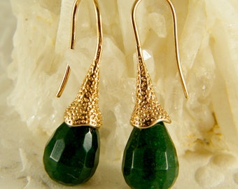 May include: A pair of gold dangle earrings with green gemstone drops. The earrings have a textured gold design and are a teardrop shape.
