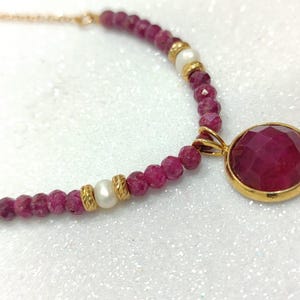 May include: A gold chain necklace with a red gemstone pendant and pink and white beads.