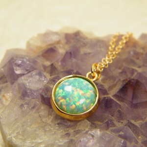 May include: A gold chain necklace with a round green opal pendant. The pendant is set in a gold bezel and has a shiny finish.