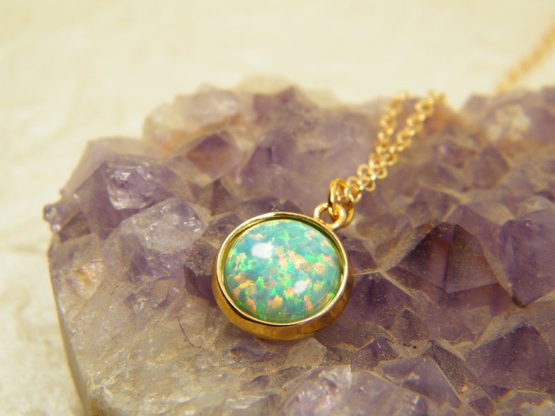 May include: A gold chain necklace with a round green opal pendant. The pendant is set in a gold bezel and has a shiny finish.