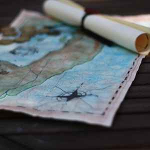 May include: A vintage-style treasure map with blue and green watercolor details, a rolled parchment, and scattered gold coins. The map features a compass rose and is tied with a black ribbon, evoking a sense of adventure and exploration.