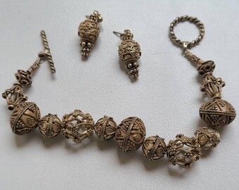 May include: A vintage jewelry set featuring a bracelet and a pair of earrings. The bracelet is composed of ornate, spherical beads with intricate detailing. The earrings mirror the design. The set is made of a gold-toned metal.