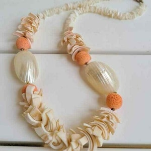 May include: A white shell necklace with orange beads and white shell accents. The necklace is made of small, irregular pieces of shell.