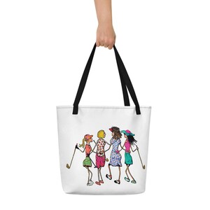 May include: A white tote bag with black handles features a cartoon illustration of four women playing golf. The women are wearing colorful clothing and hats. The illustration is in a whimsical style.