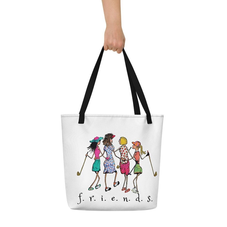 May include: White tote bag with a black handle and a cartoon image of four women playing golf. The text "f.r.i.e.n.d.s." is printed below the image.