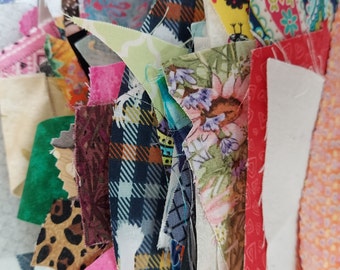 May include: A collection of colorful fabric scraps in various patterns and textures, including plaid, floral, and paisley. The scraps are arranged in a random order, creating a visually interesting and textured background.