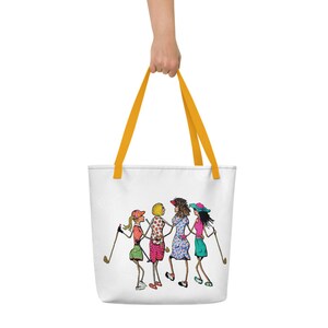May include: A white tote bag with yellow handles features a cartoon illustration of four women playing golf. The women are wearing colorful clothing and hats, and they are holding golf clubs.