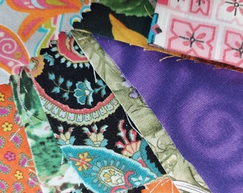 May include: A collection of colorful fabric scraps with various patterns, including paisley, floral, and geometric designs. The fabrics are arranged in a layered, overlapping pattern, creating a visually interesting and textured composition.