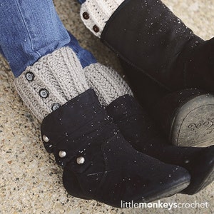 May include: Close-up of gray crochet boot cuffs with three dark buttons, worn with blue jeans and black boots. The cuffs are ribbed and appear handmade. The boots have decorative silver studs.
