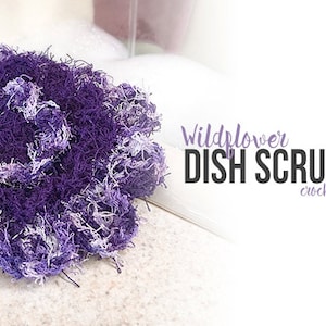 May include: A purple and white crocheted dish scrubby. The scrubby is made with a fluffy yarn and is shaped like a ball. The text "Wildflower Dish Scrubby crochet pattern" is visible in the image.
