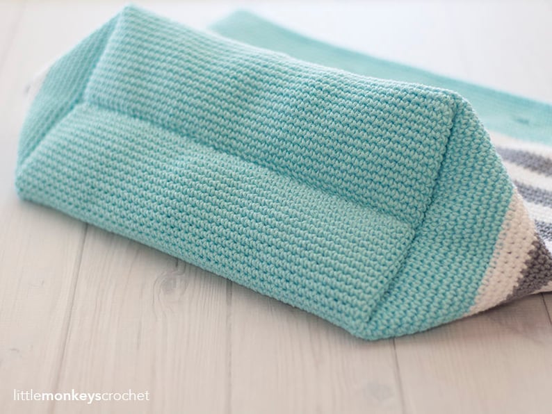 May include: A crocheted tote bag with a striped design in white, gray, and light blue. The bag is made with a textured stitch and has a flat bottom.