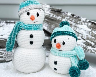 Peut inclure: Deux bonhommes de neige en crochet avec des chapeaux et des écharpes turquoise. Le plus grand bonhomme de neige a un corps blanc avec deux boutons noirs et un nez de carotte. Le plus petit bonhomme de neige a un corps blanc avec deux boutons noirs et un nez de carotte orange.