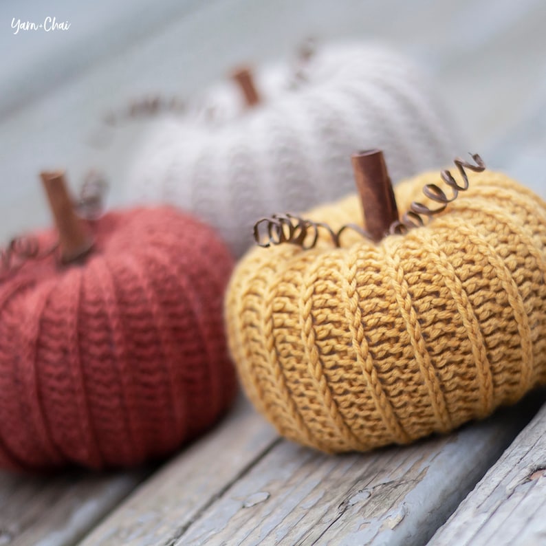 Op de afbeelding: Drie gehaakte pompoenen in verschillende kleuren: rood, geel en wit. De pompoenen zijn gemaakt met een textuur-steek en hebben draadstengels.