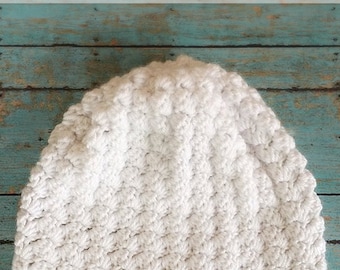 Könnte beinhalten: Weiße gehäkelte Schlappmütze mit einem strukturierten Stichmuster. Die Mütze heißt "Snowdrift Slouch" und wird von Little Monkeys Crochet hergestellt.