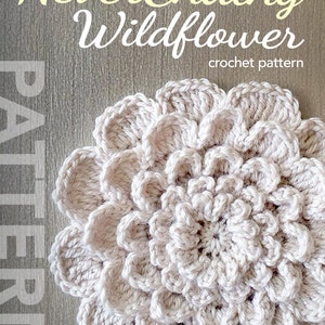 May include: The NeverEnding Wildflower crochet pattern features a large, cream-coloured crocheted flower with a spiral design. The flower is on a woodgrain background.