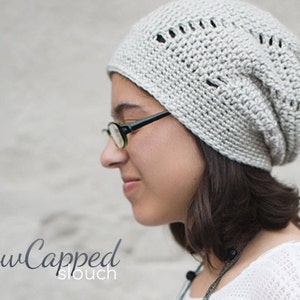 May include: A light gray crocheted beanie hat with a slouchy fit. The hat has a textured stitch pattern and decorative openings near the top. The text "SnowCapped slouch" is written in a cursive font at the bottom of the image.