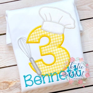 May include: White t-shirt with a yellow and white gingham number 3, a gray whisk, and a white chef's hat. The name "Benne" is embroidered in turquoise below the number. The text "katie did it CRAFTS" is in the lower right corner.