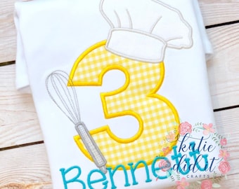 Op de afbeelding: Wit T-shirt met een geel en wit geruit nummer 3, een grijze garde en een witte koksmuts. De naam "Benne" is in turquoise onder het nummer geborduurd. De tekst "katie did it CRAFTS" staat in de rechterbenedenhoek.