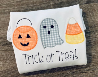 May include: White t-shirt with a pumpkin, ghost, and candy corn applique. The text "Trick or Treat" is embroidered below the appliques.