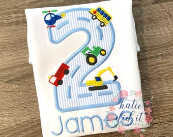May include: A white t-shirt with a blue and white striped number two, a blue helicopter, a yellow school bus, a red fire truck, a green tractor, and a yellow excavator. The name "Jam" is embroidered below the number.