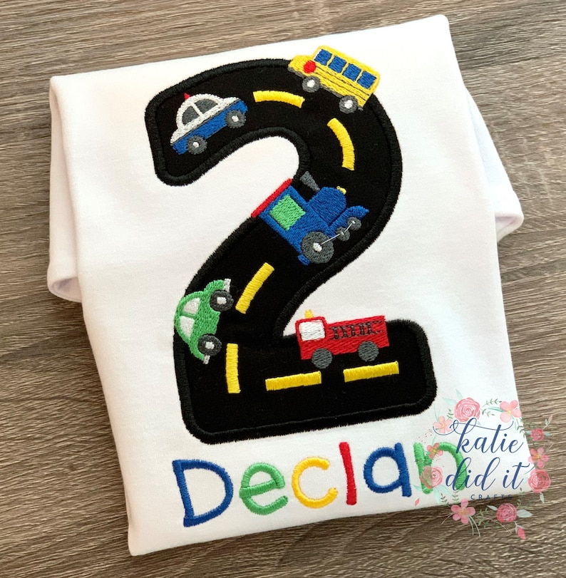 white shirt with black number 2 with embroidered vehicles driving on it. optional name below design