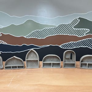 May include: A set of six gray ceramic miniature shelves with various architectural shapes, including arched, pointed, and rounded designs. Each piece features unique interior textures, small ledges, and carved patterns on the back panels.