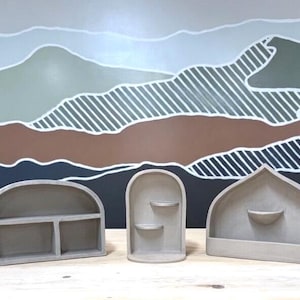 May include: Five light gray, matte-finish wall shelves of varying shapes, including arched, domed, and pointed designs. Each shelf features internal compartments or small ledges for display, constructed from a smooth, solid material.