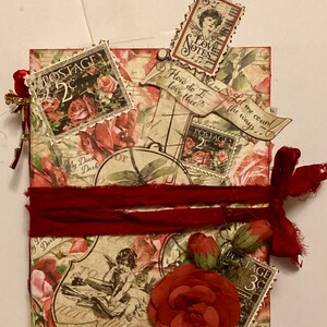 May include: A red, white, and brown scrapbook with a vintage aesthetic. The cover features a variety of decorative elements, including paper roses, postage stamps, and a ribbon. The text "How do I love thee?" and "Let me count the ways" is visible on the cover.
