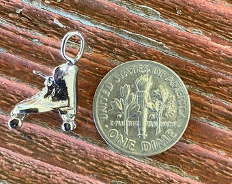 May include: A silver roller skate charm with a loop for a necklace or bracelet. The charm is next to a United States dime coin. The charm is approximately 0.75 inches long.