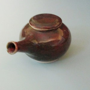 May include: A brown ceramic teapot with a lid and a spout. The teapot has a dark brown glaze with a slight sheen.