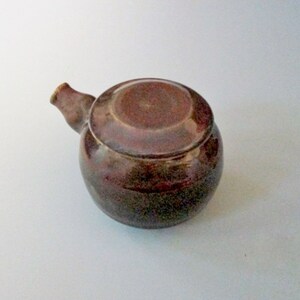 May include: A small, brown ceramic teapot with a rounded body and a small spout. The teapot has a dark brown glaze with a subtle sheen.