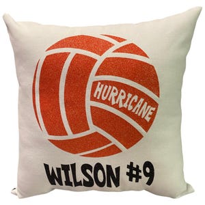 May include: White pillow with an orange volleyball graphic. The volleyball has the word "HURRICANE" written on it. Below the volleyball is the text "WILSON #9".