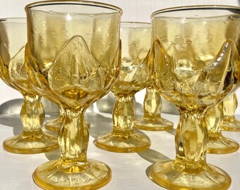 May include: Set of six yellow glass goblets with a unique, textured design. The goblets have a wide bowl and a tall, slender stem.