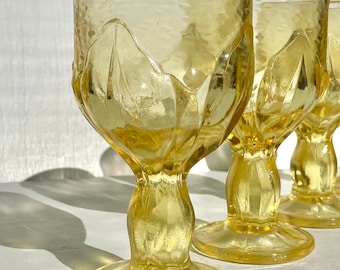 May include: Set of three yellow glass goblets with a textured, fluted design. The goblets have a wide bowl and a tall, slender stem.