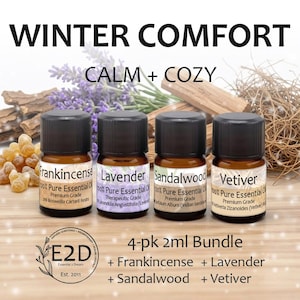 May include: A 4-pack bundle of 2ml essential oil bottles labeled Frankincense, Lavender, Sandalwood, and Vetiver. Each amber glass bottle has a black cap and white label. The text reads WINTER COMFORT CALM + COZY and 4-pk 2ml Bundle.