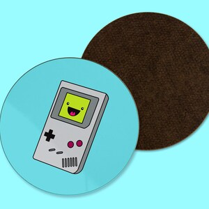 May include: A set of two round coasters. One coaster features a cartoon handheld video game with a smiling face on a light blue background. The second coaster is brown and has a textured surface. The background is light blue.