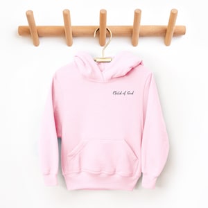 Puede incluir: Sudadera con capucha rosa con el texto "Child of God" bordado en la parte delantera.