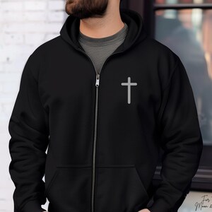 May include: A black zippered hoodie with a white cross on the front. The hoodie has a hood and a zipper closure.