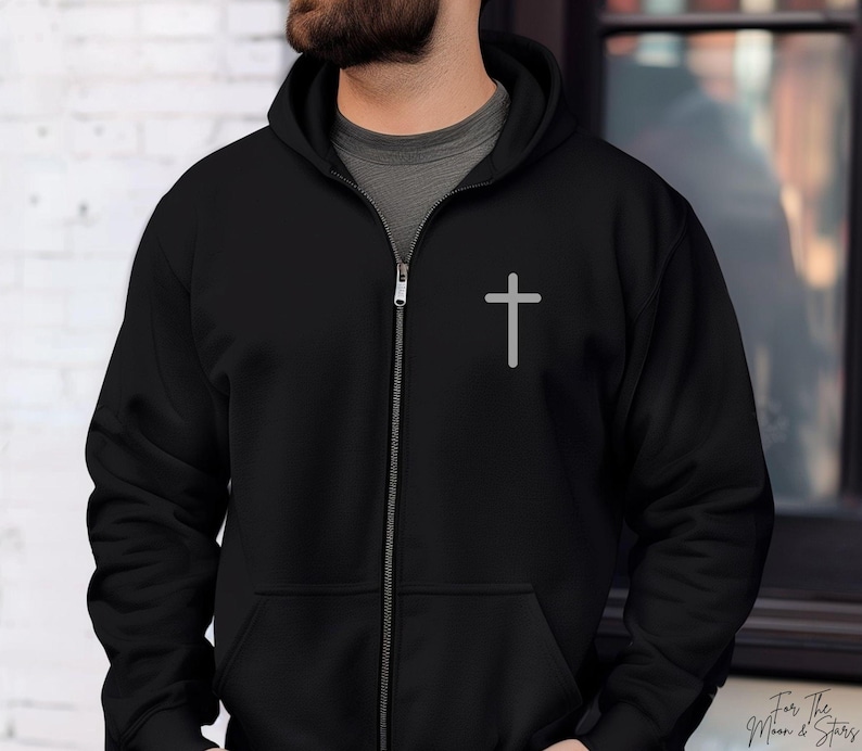 May include: A black zippered hoodie with a white cross on the front. The hoodie has a hood and a zipper closure.