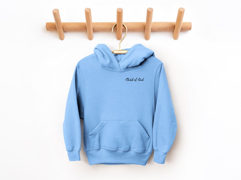 Puede incluir: Una sudadera con capucha azul claro con un bolsillo y una frase bordada en negro "Child of God" en la parte delantera.