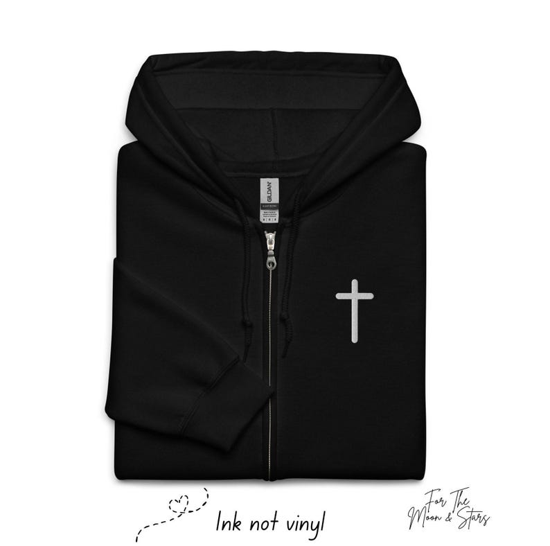 May include: Black zippered hoodie with a white cross on the front. The hoodie has a drawstring hood and a zipper closure. The text "Ink not vinyl" is written below the image.