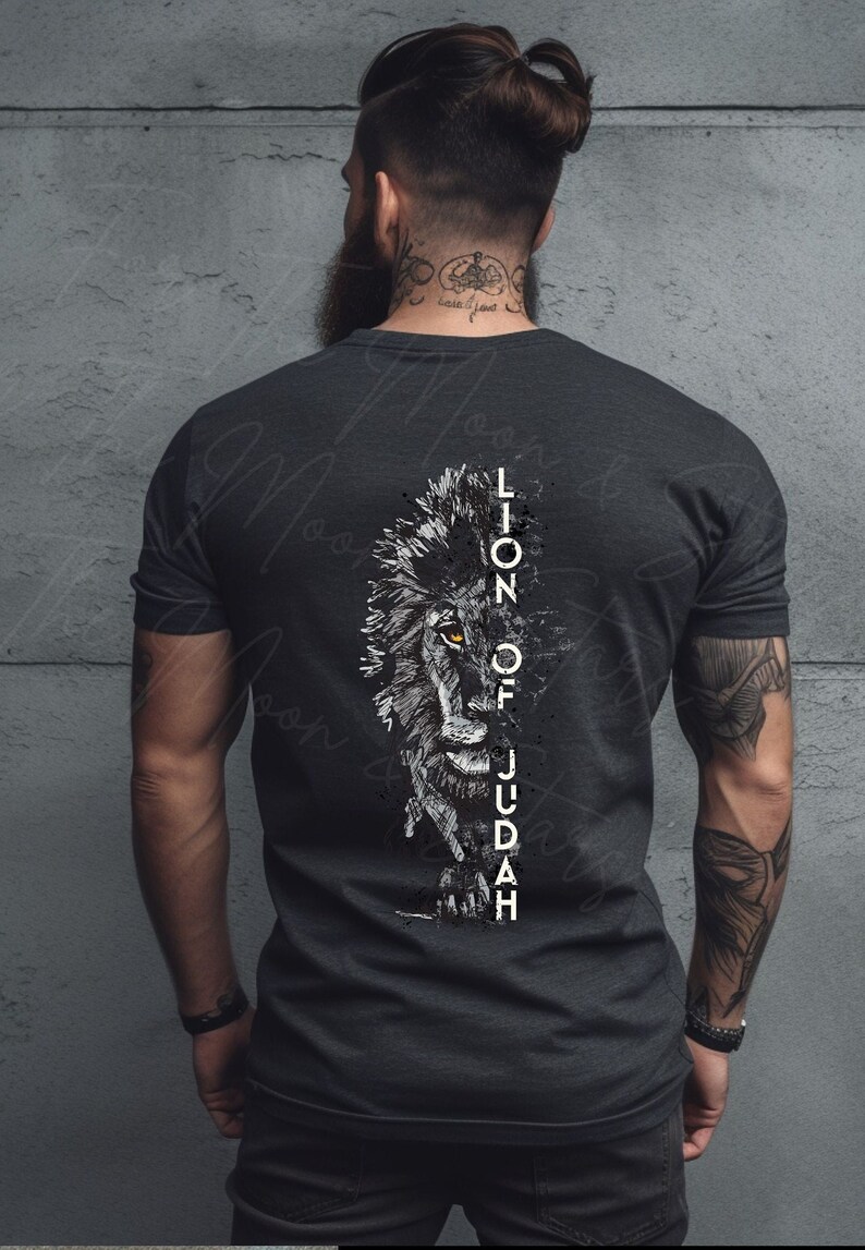Puede incluir: Una camiseta gris oscuro con un gr&aacute;fico en blanco y negro de la cara de un le&oacute;n. El texto "Lion of Judah" est&aacute; escrito verticalmente a un lado del gr&aacute;fico.
