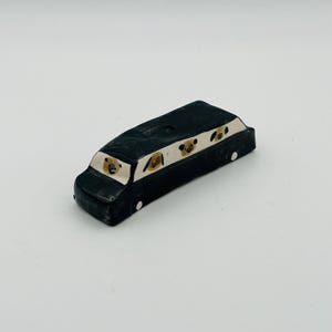 May include: A black ceramic bus with white trim and small white wheels. The bus features several dog faces in the windows. The dog faces are brown and tan with black eyes and noses. The bus is a whimsical decorative item.