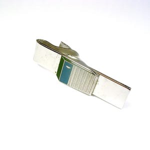 May include: Silver-toned tie clip with a rectangular design. The clip features a rectangular section with a textured pattern and a section with green and teal enamel. A classic accessory for formal wear.