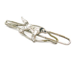 May include: A silver-toned tie clip featuring a detailed bunny rabbit design. The clip has a classic bar shape with a spring-loaded clasp. The rabbit is in a running pose, adding a touch of whimsy to the accessory.