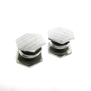 May include: Two vintage silver-toned cufflinks with a hexagonal top and base. The tops have a textured, striped pattern. The cufflinks are connected by a coiled spring mechanism. The background is white.