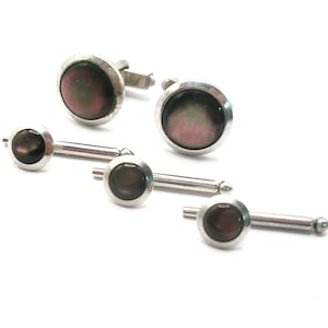 May include: A set of silver-toned cufflinks and shirt studs. The cufflinks and studs have a round, iridescent, dark-colored center stone. The set includes two pairs of cufflinks and three shirt studs, all on a white background.