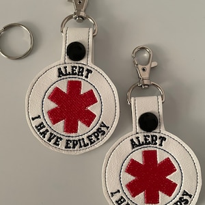 May include: Two white leather keychains with a red star of life and the text "ALERT I HAVE EPILEPSY".