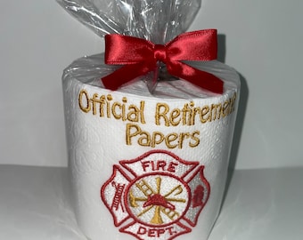 May include: A white toilet paper roll with a red ribbon and a gold embroidered message that says "Official Retirement Papers". The roll also has a red and gold embroidered fire department logo with the words "Fire Dept."